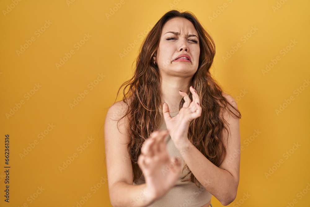Young hispanic woman standing over yellow background disgusted expression, displeased and fearful doing disgust face because aversion reaction. with hands raised - obrazy, fototapety, plakaty 