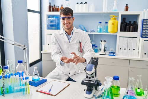 Young hispanic man scientist using sanitizer gel hands at laboratory