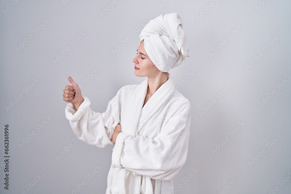 Blonde caucasian woman wearing bathrobe looking proud, smiling doing thumbs up gesture to the side Blonde caucasian woman wearing bathrobe looking proud, smiling doing thumbs up gesture to the side