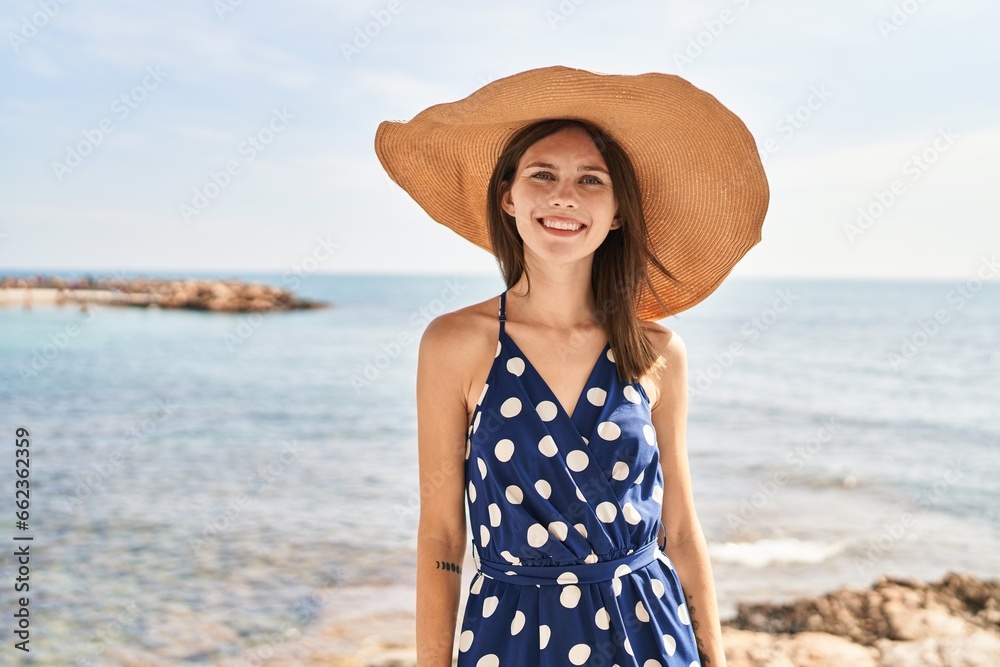 Young blonde woman tourist smiling confident wearing summer hat at beach