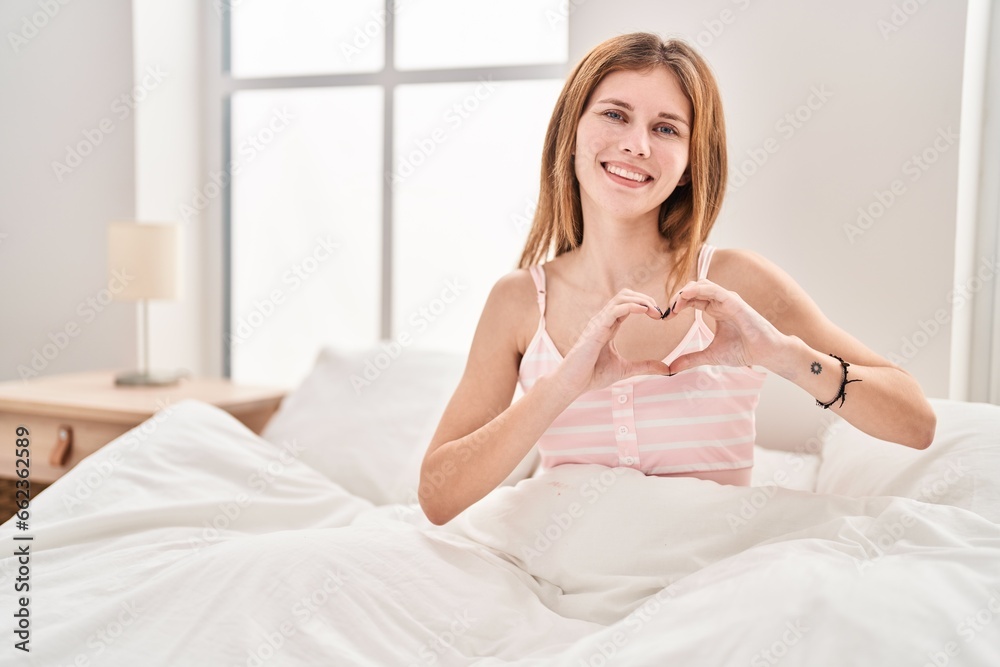 Young blonde woman doing heart gesture sitting on bed at bedroom Young blonde woman doing heart gesture sitting on bed at bedroom