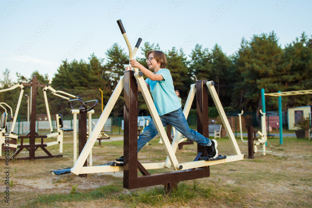 Fototapeta premium Healthy summer holidays. An active child boy is doing exercises on the sports ground in the park. Sport and active rest for children