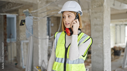Young blonde woman architect talking on smartphone at construction site