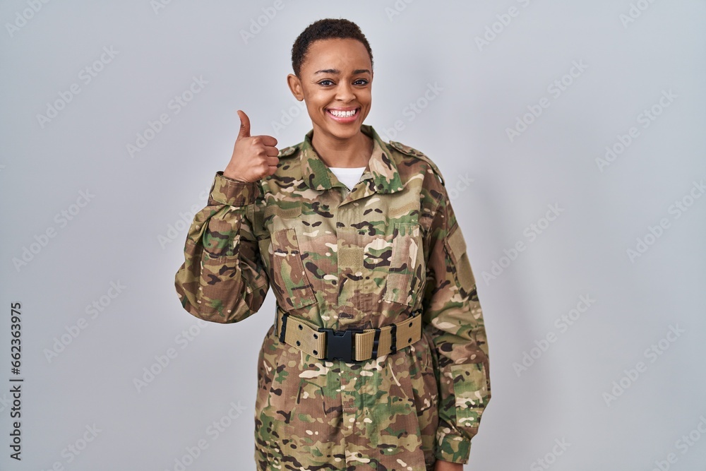Beautiful african american woman wearing camouflage army uniform doing happy thumbs up gesture with hand. approving expression looking at the camera showing success.