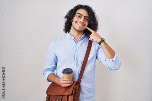 Hispanic man with curly hair drinking a cup of take away coffee smiling cheerful showing and pointing with fingers teeth and mouth. dental health concept.