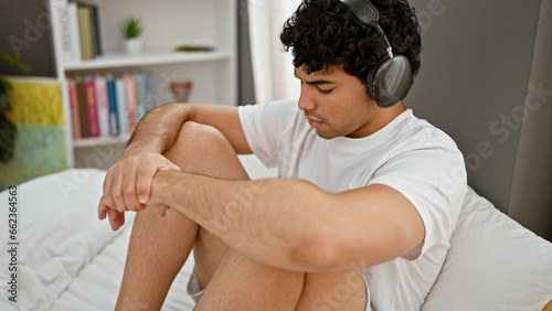 Young latin man listening to music relaxed on bed at bedroom