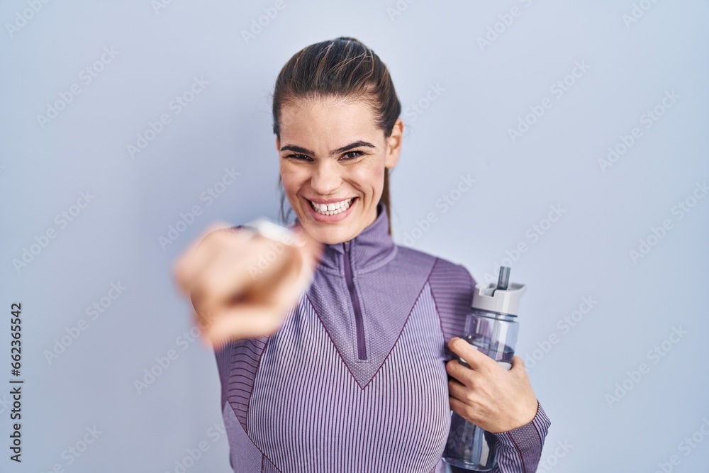 Beautiful woman wearing sportswear holding water bottle pointing to you and the camera with fingers, smiling positive and cheerful Beautiful woman wearing sportswear holding water bottle pointing to you and the camera with fingers, smiling positive and cheerful