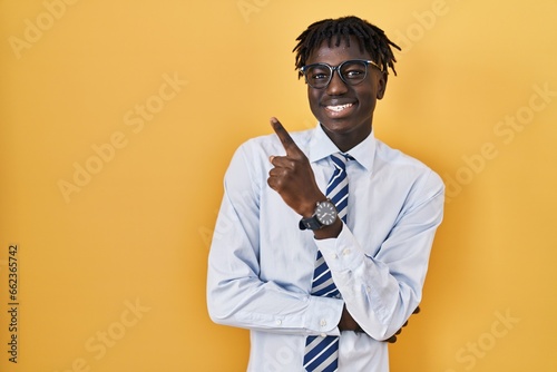 Valokuva African man with dreadlocks standing over yellow background with a big smile on face, pointing with hand and finger to the side looking at the camera