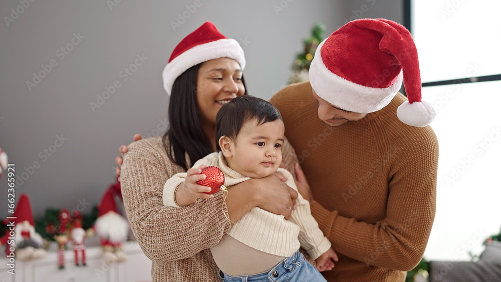 Couple and son holding decoration ball standing by christmas tree at home Couple and son holding decoration ball standing by christmas tree at home