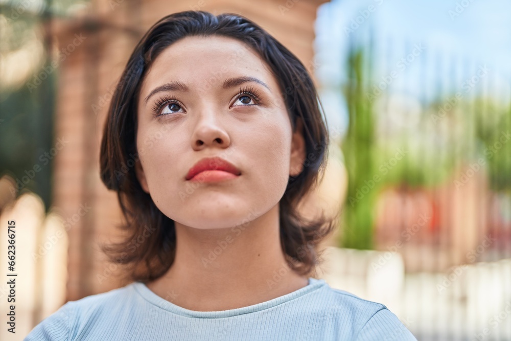 Young hispanic woman looking to the sky with serious expression at street Young hispanic woman looking to the sky with serious expression at street