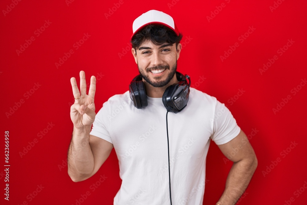 Hispanic man with beard wearing gamer hat and headphones showing and pointing up with fingers number three while smiling confident and happy. Hispanic man with beard wearing gamer hat and headphones showing and pointing up with fingers number three while smiling confident and happy.