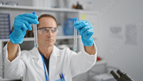 Hispanic middle age man, a serious scientist engrossed in his experiment, securely handles test tubes in his lab, carefully measuring liquid samples for medical research with intense concentration.