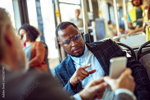 Young businessman pointing on a smartphone of his colleague while riding the bus photo