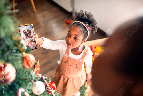 Young girl showing her grandparents the Christmas tree on a video call from a smartphone at home photo