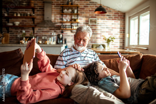 Grandfather bonding with his grandchildren while they use electronics on the couch at home photo