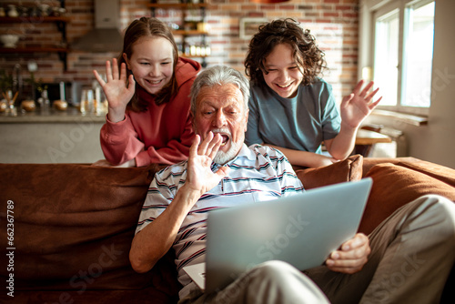 Grandfather video calling with his grandchildren on the couch at home photo