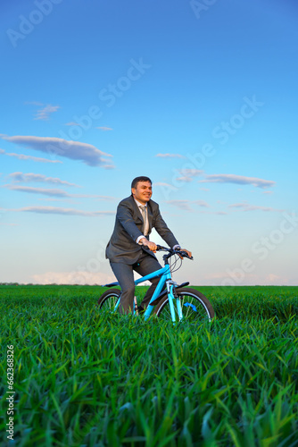 Fototapeta Naklejka Na Ścianę i Meble -  businessman rides a bicycle through a green grass field, the concept of activity, leisure or freelancing