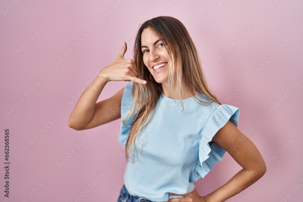 Young hispanic woman standing over pink background smiling doing phone gesture with hand and fingers like talking on the telephone. communicating concepts. Young hispanic woman standing over pink background smiling doing phone gesture with hand and fingers like talking on the telephone. communicating concepts.