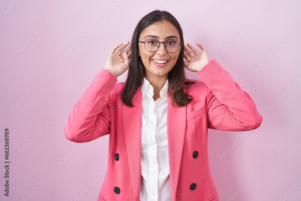 Young hispanic woman wearing business clothes and glasses smiling pulling ears with fingers, funny gesture. audition problem