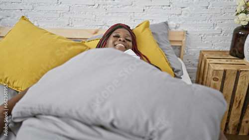 Foto Exhausted african american woman in braids, comfortably lying on a cozy bed, falling asleep in her warm, relaxing bedroom, surrendering to the sweet call of sleep after a tiresome day