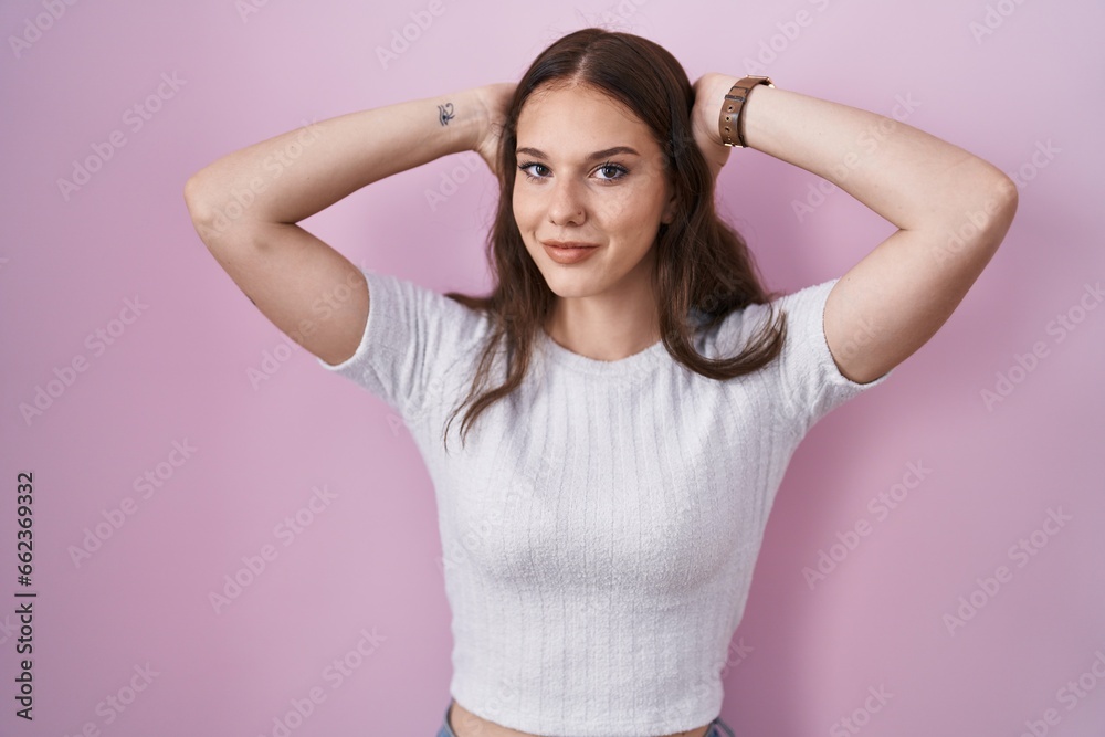 Young hispanic girl standing over pink background relaxing and stretching, arms and hands behind head and neck smiling happy