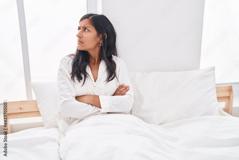 Young beautiful hispanic woman sitting on bed with unhappy expression and arms crossed gesture at bedroom Young beautiful hispanic woman sitting on bed with unhappy expression and arms crossed gesture at bedroom