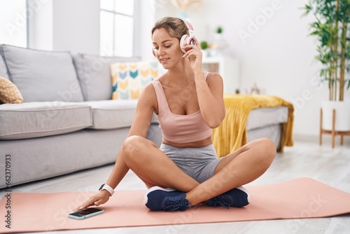 Young blonde woman listening to music sitting on floor at home