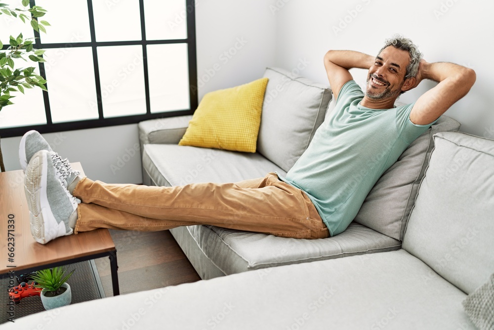 Middle age grey-haired man relaxed with hands on head sitting on sofa at home Middle age grey-haired man relaxed with hands on head sitting on sofa at home