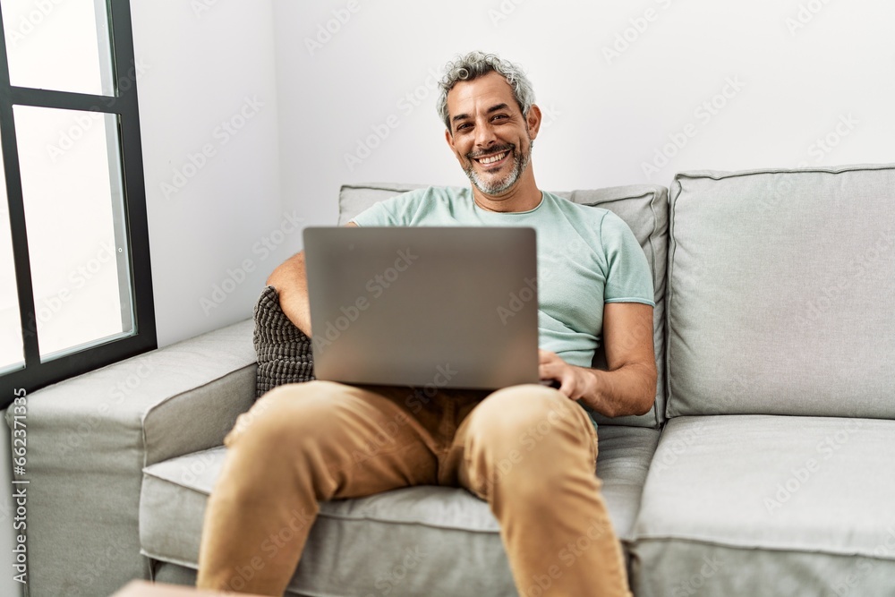 Middle age grey-haired man using laptop sitting on sofa at home Middle age grey-haired man using laptop sitting on sofa at home