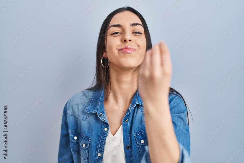 Hispanic woman standing over blue background doing italian gesture with hand and fingers confident expression - obrazy, fototapety, plakaty 