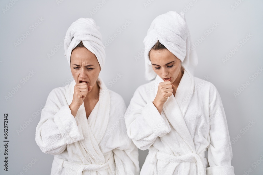 Middle age woman and daughter wearing white bathrobe and towel feeling unwell and coughing as symptom for cold or bronchitis. health care concept. Middle age woman and daughter wearing white bathrobe and towel feeling unwell and coughing as symptom for cold or bronchitis. health care concept.