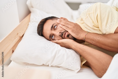 Young hispanic man stressed lying on bed at bedroom