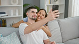 Beautiful couple making fun selfie memories on sofa, confidently smiling and expressing love at their cozy home