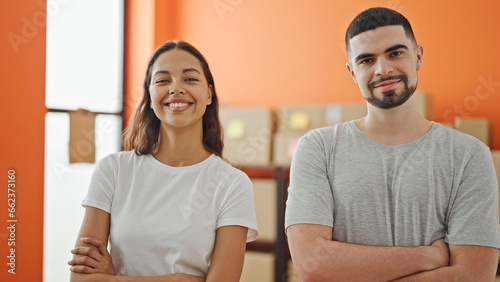 Two confident workers, man and woman, together smiling with arms crossed at their workplace