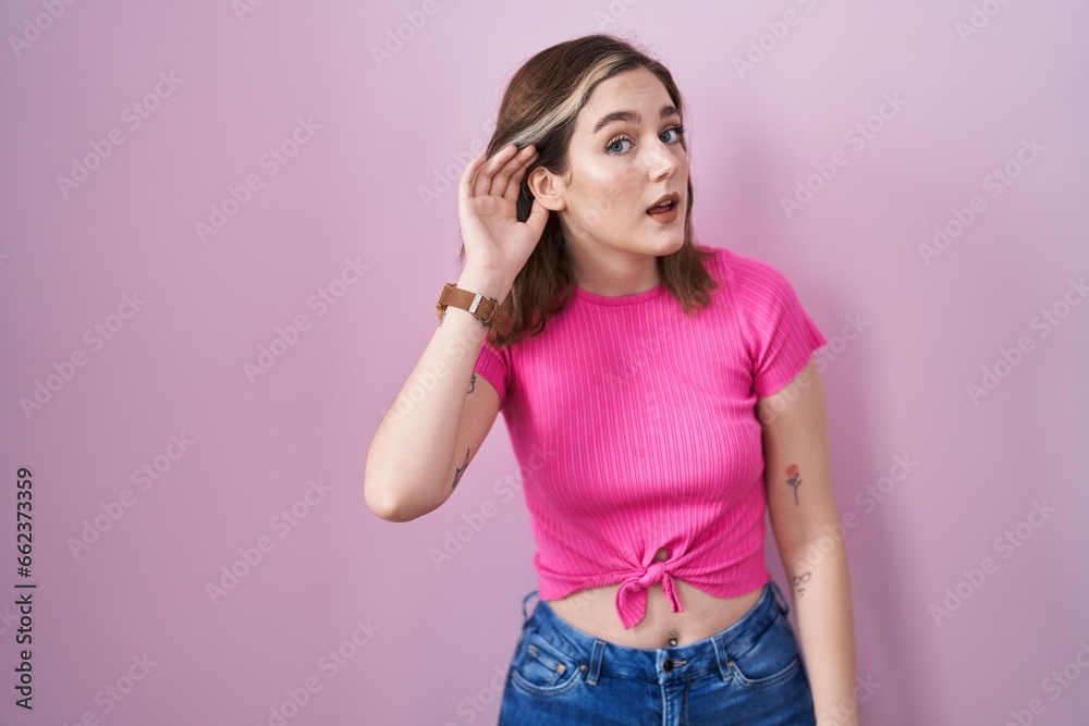 Blonde caucasian woman standing over pink background smiling with hand over ear listening an hearing to rumor or gossip. deafness concept. Blonde caucasian woman standing over pink background smiling with hand over ear listening an hearing to rumor or gossip. deafness concept.
