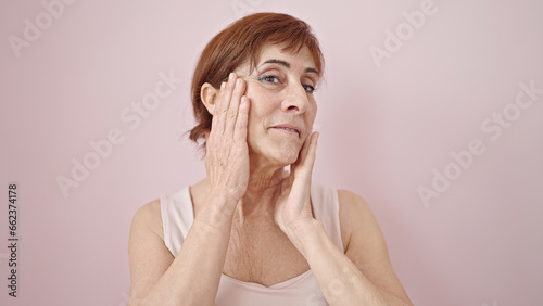 Mature hispanic woman looking serious touching face with hand over isolated pink background