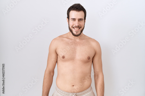 Young hispanic man standing shirtless over white background with a happy and cool smile on face. lucky person.