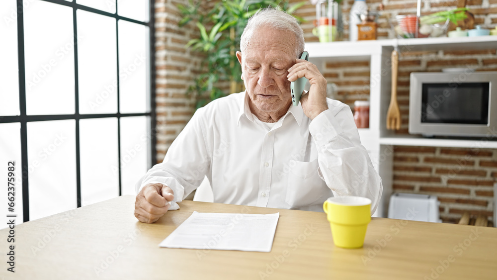 Senior grey-haired man angry arguing on smartphone sitting on table at dinning room Senior grey-haired man angry arguing on smartphone sitting on table at dinning room
