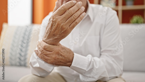 Senior grey-haired man sitting on sofa suffering for wrist pain at home