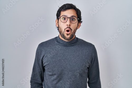 Handsome latin man standing over isolated background in shock face, looking skeptical and sarcastic, surprised with open mouth © Krakenimages.com