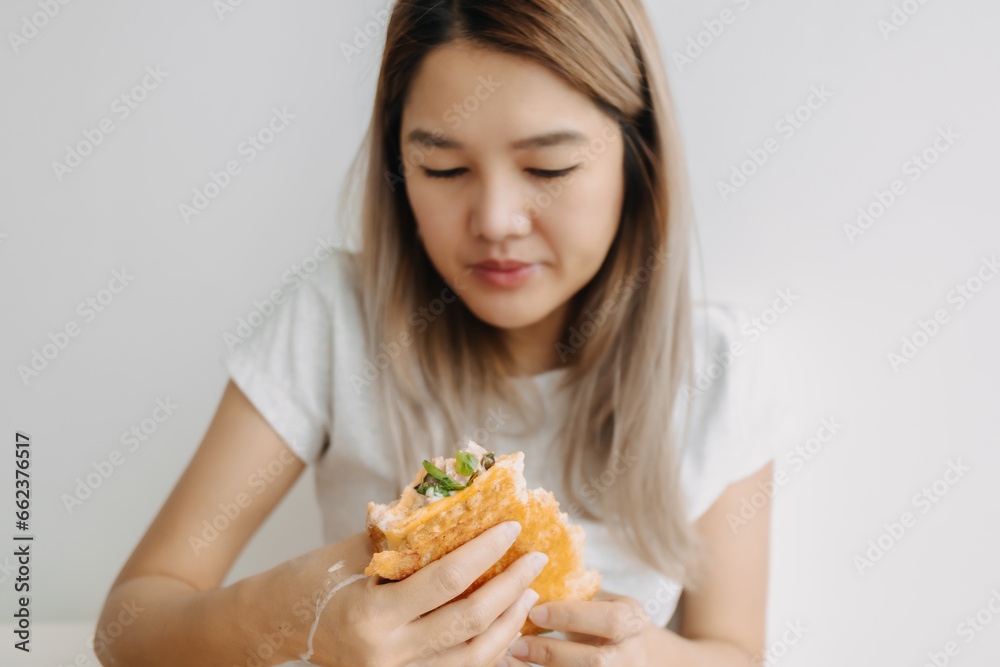 Close up of Asian Thai woman having homemade breakfast sandwich hungrily at home alone isolated on white wall. Close up of Asian Thai woman having homemade breakfast sandwich hungrily at home alone isolated on white wall.