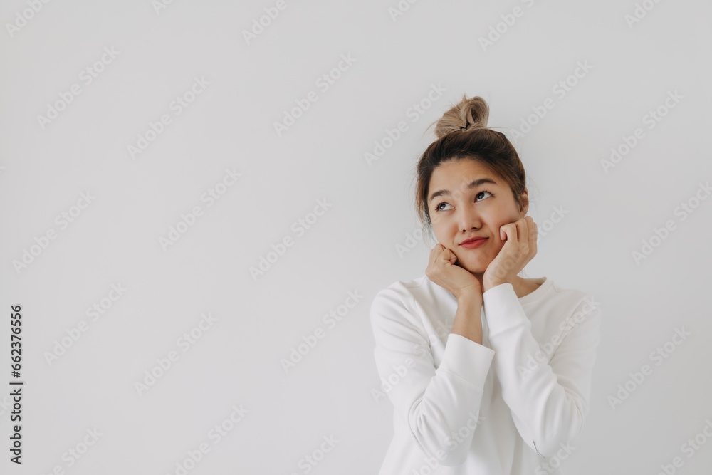 Asian Thai woman with bun hair wear sweater, cute gesture, having day dream, wishing something, looking above isolated over white background wall in winter. Asian Thai woman with bun hair wear sweater, cute gesture, having day dream, wishing something, looking above isolated over white background wall in winter.