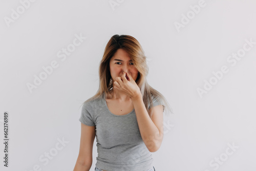 Fotografía Unhappy Asian Thai woman wear grey, squeezing, pinching and holding nose blocking bad smell, smelly isolated on white background wall