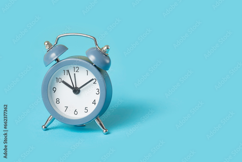 Close up one small blue metal twin bell retro alarm clock over light blue background with copy space, low angle front view Close up one small blue metal twin bell retro alarm clock over light blue background with copy space, low angle front view