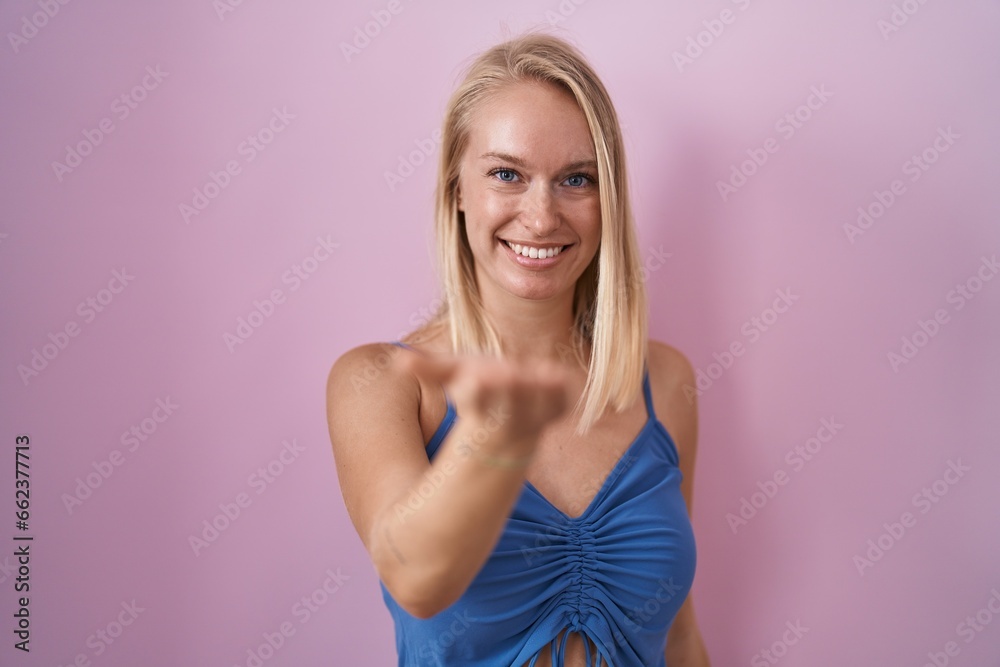 Young caucasian woman standing over pink background smiling cheerful offering palm hand giving assistance and acceptance. Young caucasian woman standing over pink background smiling cheerful offering palm hand giving assistance and acceptance.