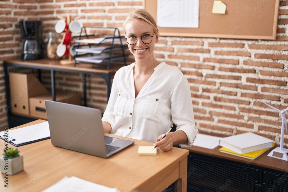 Young blonde woman business worker using laptop writing on reminder paper at office Young blonde woman business worker using laptop writing on reminder paper at office