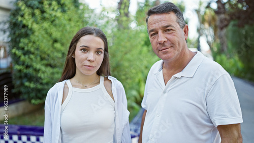 Confident father and his lovely daughter, two happy family members, standing together, enveloped in sunny park sunlight, joyfully smiling. their casual expression reflecting pure love and positivity.