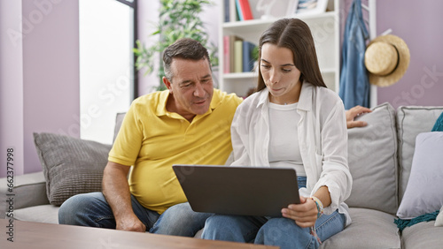 Joyful father and daughter sitting on a comfortable sofa, using their laptop, and sharing a heartwarming smile at home