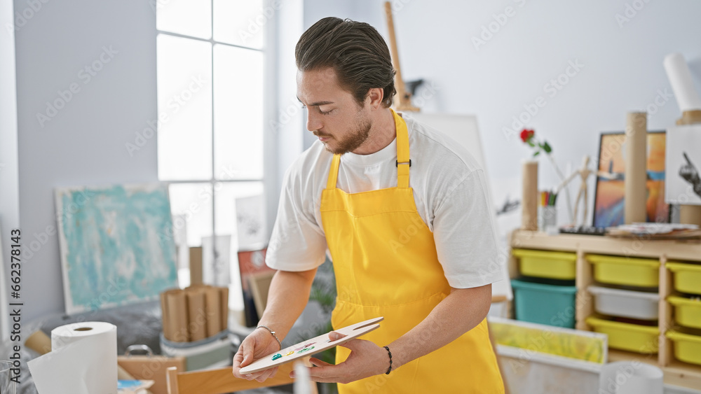 Young hispanic man artist holding paintbrush and palette at art studio Young hispanic man artist holding paintbrush and palette at art studio