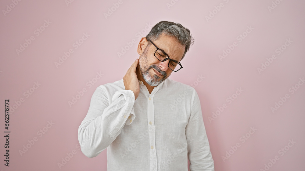 Stressed out young hispanic man, grey-haired and handsome, battling crippling cervical back ache over isolated pink background